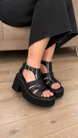 Sandalias de cuero color suela, con plataforma alta y taco ancho. Presentan tiras cruzadas en el empeine con mix de texturas y cierre de hebilla metálica en el tobillo.