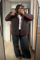Chaqueta reversible de paño, con un lado gris oscuro con costuras decorativas en hilo rojo y el otro lado con estampado de cuadros. Presenta corte holgado, mangas largas y diseño abierto.
