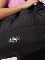 Bolso tipo tote bag de diseño acolchado en color negro, con correas ajustables y cierre lateral. Presenta el logo de la marca Rusty en la parte frontal.