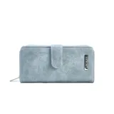 Billetera larga de cuerina color celeste con efecto desgastado, solapa con broche a presión y placa metálica con la marca grabada. Cuenta con compartimento posterior con cierre metálico.