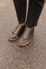 Zapatillas acordonadas de cuero color negro con suela marrón. Diseño artesanal de producción local.