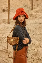 Bandolera con silueta de media luna y estructura rígida, confeccionada en cuero con estampado animal print tipo vaca. Presenta herrajes metálicos en tono bronce, cierre superior y correa regulable que permite su uso al hombro o cruzada. Incluye una placa metálica decorativa con iniciales en el frente.