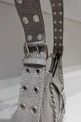 Cartera tipo baguette negra de cuero vacuno con textura tipo piel de cocodrilo. Tiene correa de cuero ajustable con detalles de tachas y cadena metálica plateada. El frente presenta un aplique de cuero con hebilla metálica plateada con tachas.
