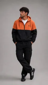 Conjunto deportivo compuesto por una campera rompevientos bicolor en naranja y negro con capucha y cierre frontal, y un pantalón cargo negro de corte recto con bolsillos laterales.