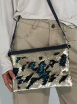 Cartera tipo sobre con lentejuelas doradas y negras reversibles, con borde superior de cuero negro y correa fina de cuero negro.