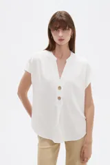 Blusa de viscosa color blanco, de corte holgado, con cuello en V y cierre frontal parcial de botones grandes con efecto carey.
