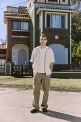 Camisa de manga corta a rayas verticales color crudo y verde, con cuello resort, corte holgado y cierre frontal con botones.