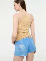 Top de tirantes color beige con tejido acanalado y sisas profundas. Presenta un pequeño emblema bordado con la palabra "Me" y una corona en el frente. El escote es redondeado en la parte delantera y recto en la espalda.