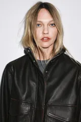 Chaqueta bomber de cuero negro con cuello alto, manga larga con cremalleras metálicas, bolsillos de plastrón con solapa y botón en delantero, bajo acabado en elástico y cierre frontal con cremallera y botones a presión ocultos por solapa.
