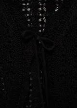 Cardigan de punto calado color negro, con mangas cortas, cuello en pico y cierre frontal mediante lazo fino. Diseño corto y ajustado.