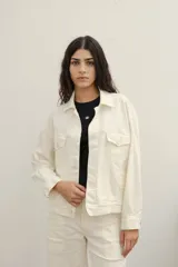 Campera de jean color crudo, con cuello camisero, cierre frontal con botones y bolsillos con solapa en el pecho.
