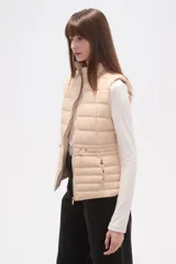 Chaleco acolchado negro, sin mangas, con cuello alto y cierre frontal con cremallera dorada. Presenta cordones ajustables a la altura de la cintura.