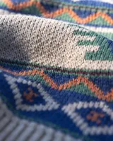 Buzo tejido de punto con diseño geométrico inspirado en motivos andinos, en tonos beige, verde, azul y naranja. Presenta cuello redondo, puños y ruedo acanalados, y etiqueta de marca en el frente.