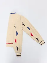 Sweater de punto con diseño de ochos en color verde, cuello redondo con detalle de franja en contraste, y apliques de rombos en las mangas. Presenta un bordado con la letra M en el pecho.