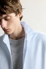 Camisa slim fit de algodón color celeste con sutil patrón de cuadros, cuello clásico y manga larga con puños abotonados.