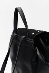 Mochila negra de símil cuero texturizado con tapa en acabado gamuzado, decorada con apliques de tachas metálicas. Tiene asa superior y correas regulables.