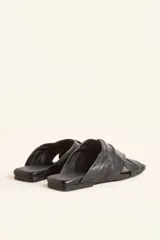 Sandalia tipo slide de cuero vacuno color blanco, con diseño de tiras cruzadas y fruncidas. Presenta una puntera cuadrada y una suela plana de cuero con un pequeño taco de 2 cm.