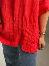 Blusa roja de lino, con cuello redondo, mangas 3/4 con presilla y botones, y diseño holgado con pliegues frontales.