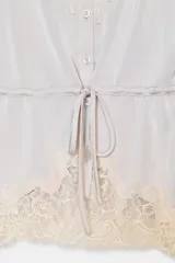 Top satinado color celeste con escote en pico y tirantes finos. Presenta detalles de encaje gris en el escote y el bajo, y una cintura ajustable con lazada.