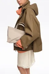 Bolso shopper mediano de mano Bimba y Lola color marrón, confeccionado en poliamida con detalles en cuero y herrajes metálicos dorados. Cuenta con doble asa de mano, correa de hombro ajustable de lona beige, cierre superior con cremallera y logo impreso en dorado al frente.