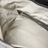 Cartera de hombro tipo hobo confeccionada en cuero negro con acabado brillante. Presenta dos cierres verticales decorativos en el frente, correa ajustable y placa metálica con logo en la parte central.