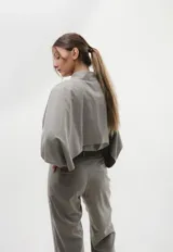 Camisa de seda peletizada con diseño de capa integrada, cuello mao y mangas abullonadas. Presenta cierre frontal con botones al tono y una estructura unida en cuello, puños y cartera.