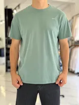 Remera de corte clásico, de color verde, con cuello redondo y mangas cortas. Presenta un pequeño estampado con las letras "SBCH" en el lado izquierdo del pecho.