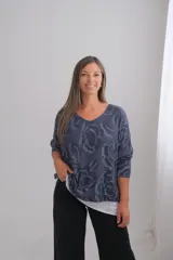 Sweter de punto con diseño de flores estampadas en tonos azules, con cuello en V y mangas tres cuartos. Presenta un diseño de doble capa con un borde inferior en color blanco que sobresale.