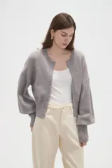 Saco de punto color beige, con cuello redondo, cierre frontal con botones y mangas largas con puños acanalados.