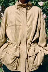 Chaqueta de efecto ante con cuello alto, manga larga y cierre frontal oculto por solapa con botones. Cuenta con bolsillos delanteros de plastrón con solapa y cintura ajustable con cordones.