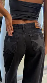 Pantalón de jean negro de calce wide leg y tiro medio, con detalle de estrellas brillantes en los bolsillos traseros.