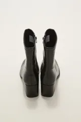 Bota corta de caña media en color negro, confeccionada en eco cuero con acabado brillante. Presenta cierre lateral interno, costura central decorativa en el empeine y taco cuadrado de altura media.