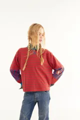 Remera de manga larga con corte boxy, confeccionada en algodón. Presenta un diseño de rayas horizontales en tonos rojos y marrones, con detalles de rayas verticales en azul y rojo en la zona de los codos. Incluye puños, tajos laterales y logo bordado en el pecho.