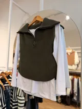 Chaleco de punto acanalado en color verde oliva, con cuello polo y cierre frontal parcial. Presenta un diseño sin mangas con corte redondeado en el ruedo.