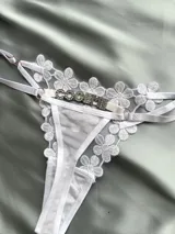 Tanga blanca regulable con detalles de encaje con diseño de flores, tiras ajustables y aplicación de letras con strass en la parte frontal.