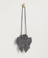 Bolso tipo bandolera de terciopelo gris, con diseño flexible y sin estructura, decorado con un lazo grande frontal y asa fruncida.