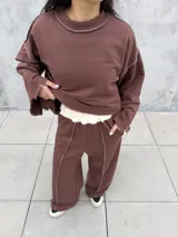 Buzo oversize de color marrón chocolate, con cuello redondo, mangas anchas y diseño con costuras expuestas en contraste. Presenta terminaciones desflecadas en el ruedo y en los puños.