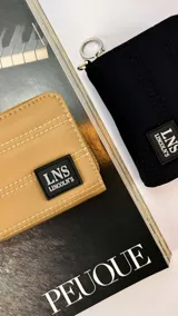 Billetera corta con cierre perimetral y tapa, confeccionada en tela capitoneada. Cuenta con compartimentos internos para tarjetas, bolsillos y correa de mano desmontable.