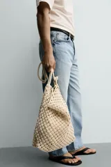 Bolso de hombro confeccionado en tejido trenzado de algodón con diseño de macramé, asa de hombro con detalle de nudo y bolsillo interior plano.