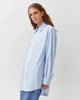 Camisa de corte recto y silueta ligeramente oversize, color celeste, con cuello clásico, cierre frontal de botones, bolsillo aplicado en el pecho y bajo redondeado.