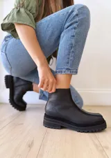 Botas negras de cuero con caña baja, cierre lateral con cremallera y suela track.