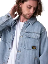 Chaqueta de denim azul claro de corte clásico, con cierre frontal de botones metálicos, cuello camisero y dos bolsillos con solapa en el pecho.