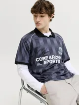 Camiseta tipo polo de manga corta con diseño de rayas verticales en tonos gris y negro. Presenta cuello polo negro, escudo deportivo en el pecho y estampa frontal con texto en color blanco. Confeccionada en tejido técnico de poliéster con corte holgado.