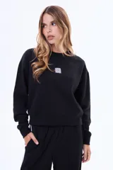 Buzo de felpa color negro con cuello redondo y ajuste holgado. Presenta un pequeño parche cuadrado con estampado a cuadros en el centro del pecho.