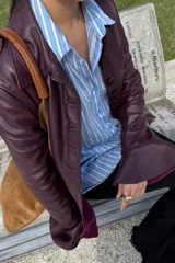 Tapado de cuero ovino color vino, con diseño de corte entallado, mangas largas con volados en los puños y ruedo con volados. Presenta cierre frontal con botones y bolsillos laterales con solapa.