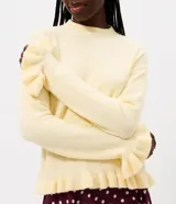 Suéter de tricot color amarillo claro, de manga larga y cuello redondo. Presenta detalles de volados acanalados en el ruedo y en los puños.