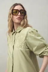 Camisa verde con bordado floral en el frente, cuello clásico, mangas largas abullonadas y cierre frontal con botones.