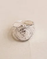 Anillo sello ajustable de acero con placa circular grabada y detalles en relieve en los laterales y la banda.
