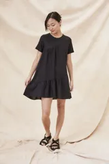 Vestido negro corto con cuello redondo, mangas cortas y falda con volantes.