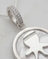 Dije circular de plata 925 con centro de nácar y silueta de niño en relieve. El pasante está decorado con circonias brillantes y se presenta con una cadena de plata fina.